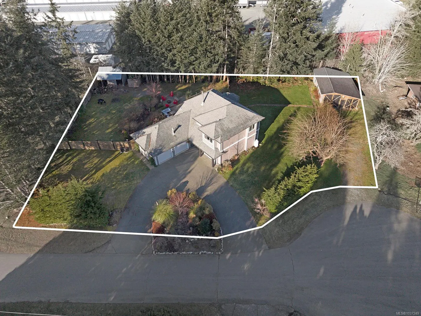 Aerial view of a two-story house with a gray roof, surrounded by trees and a white property line. A circular driveway leads to a two-car garage.