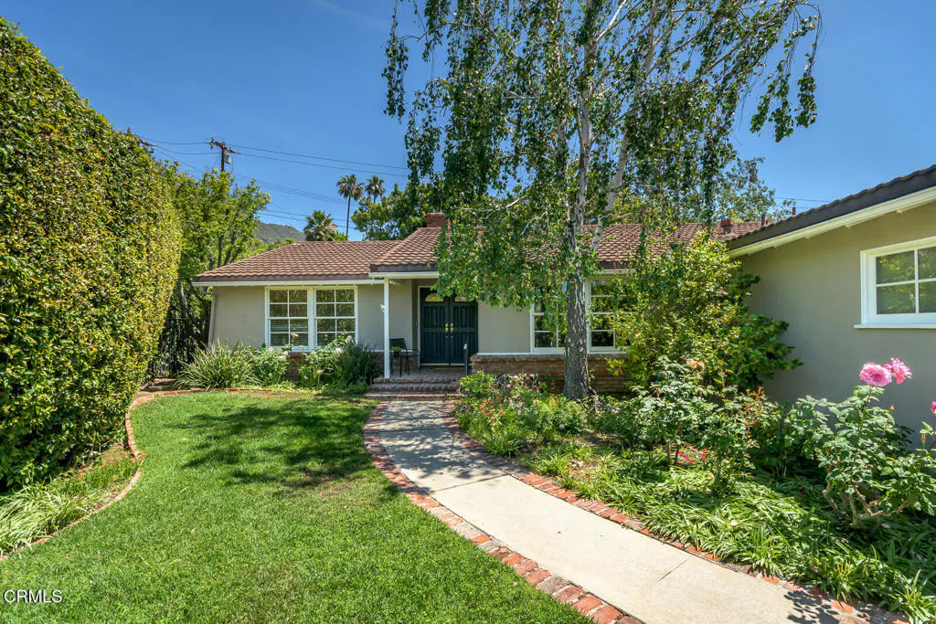 Front view of a single-story house with a brown roof, green lawn, and a concrete walkway lined with red bricks.