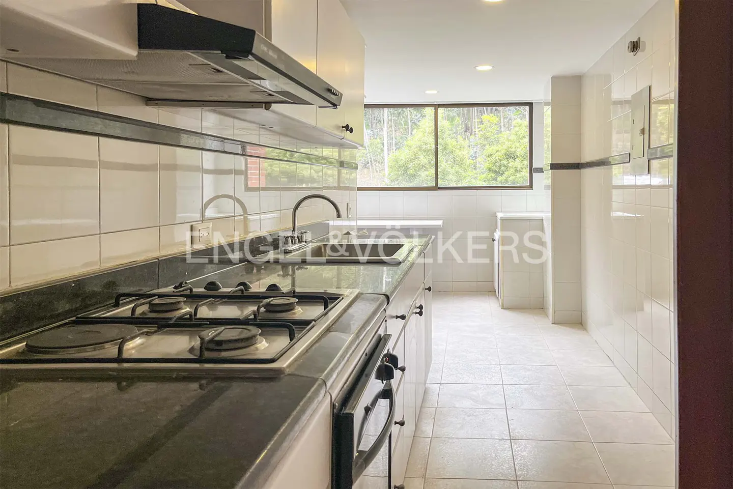 A bright kitchen with white cabinets, black countertops, and a gas stove. A window overlooks a green, wooded area.