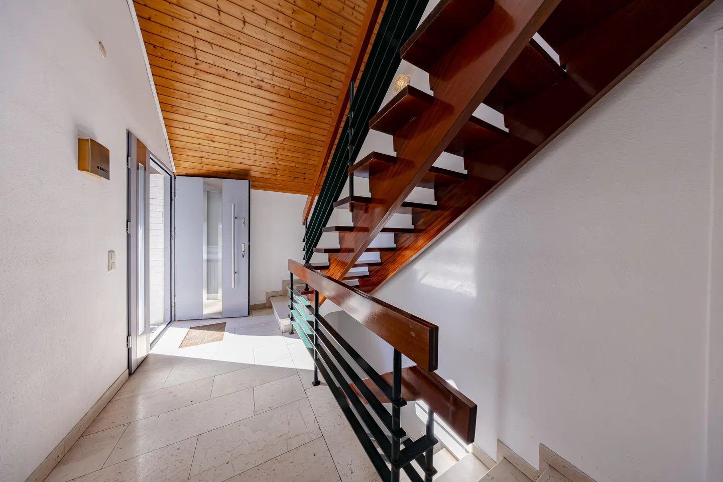 Entryway with open front door, wood ceiling, and staircase with wood steps and black metal railing.