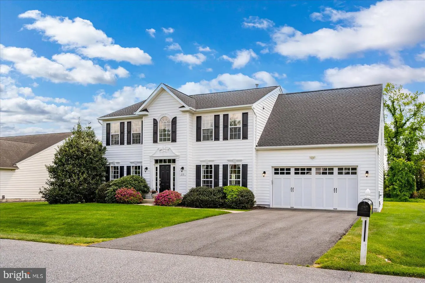 Two-story white house with black shutters, a gray roof, and a two-car garage on a green lawn under a blue sky.