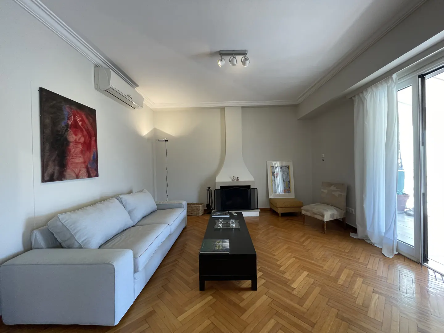 Living room with herringbone wood floors, a white sofa, black coffee table, and a fireplace. Art hangs on the wall.