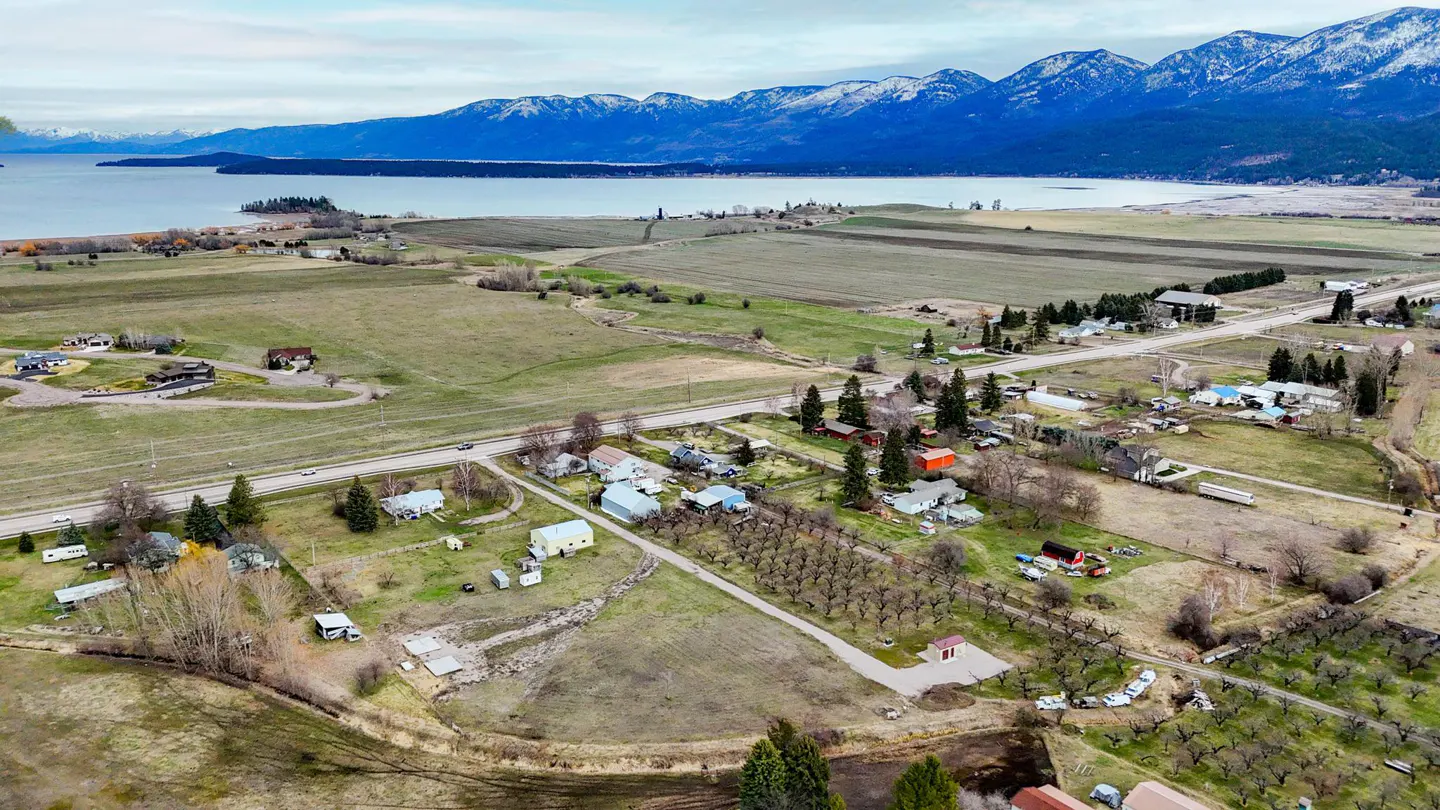 Aerial view of a rural town with houses, fields, and a lake with mountains in the background.