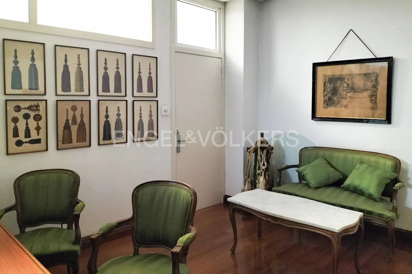 A room with green chairs, a sofa, and tassel art on the wall.