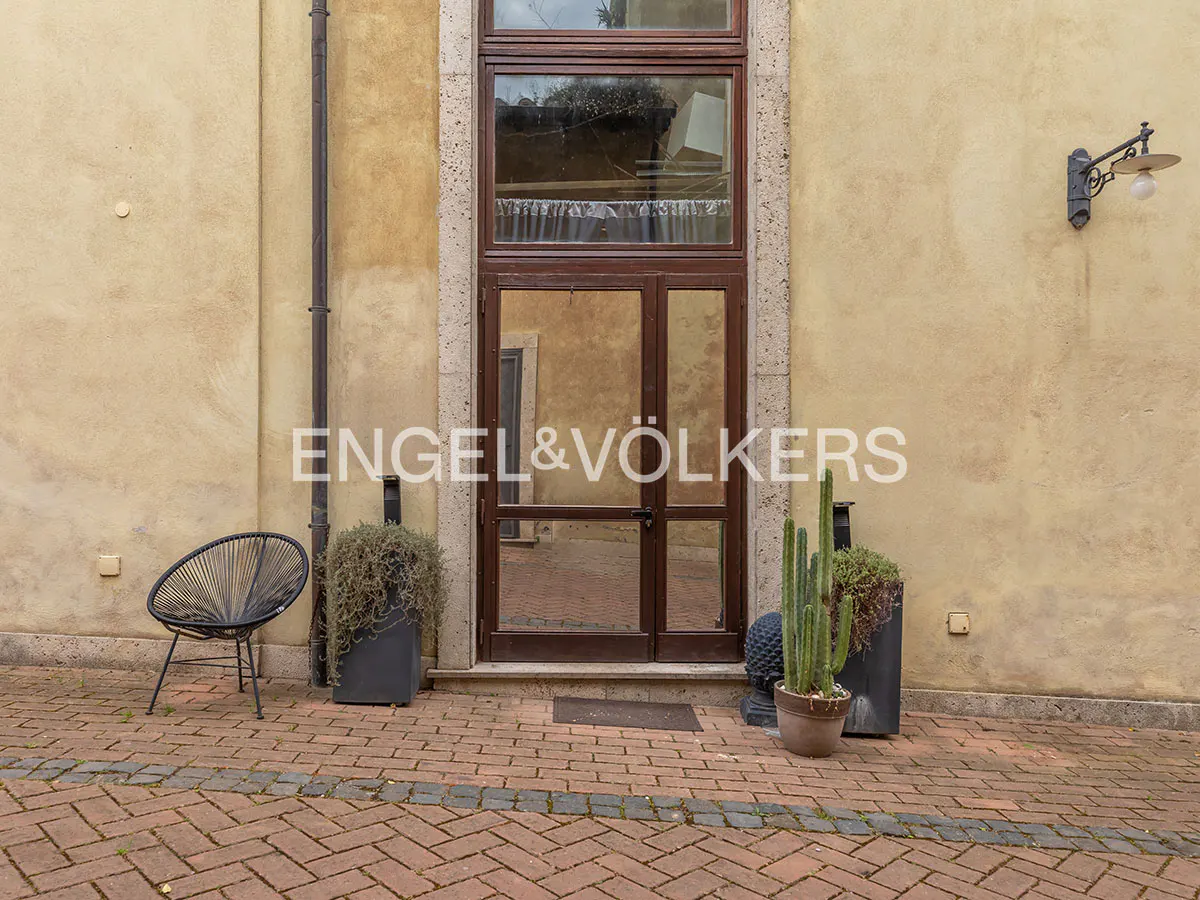 Exterior view of a building with a brown door, plants, and a chair on a brick patio.