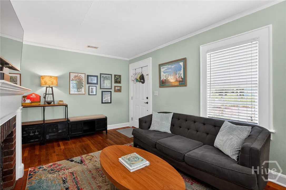 Living room with light green walls, dark gray sofa, wood floors, and a colorful rug. A wooden coffee table sits in front of the sofa.