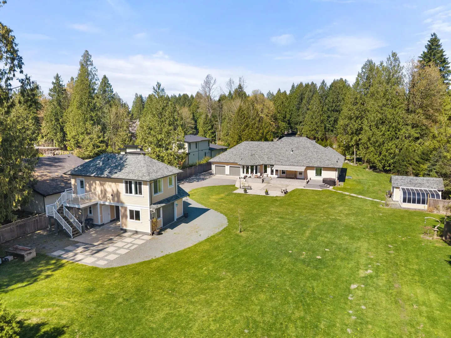 Aerial view of a tan two-story house and a larger one-story house with a green lawn and trees.