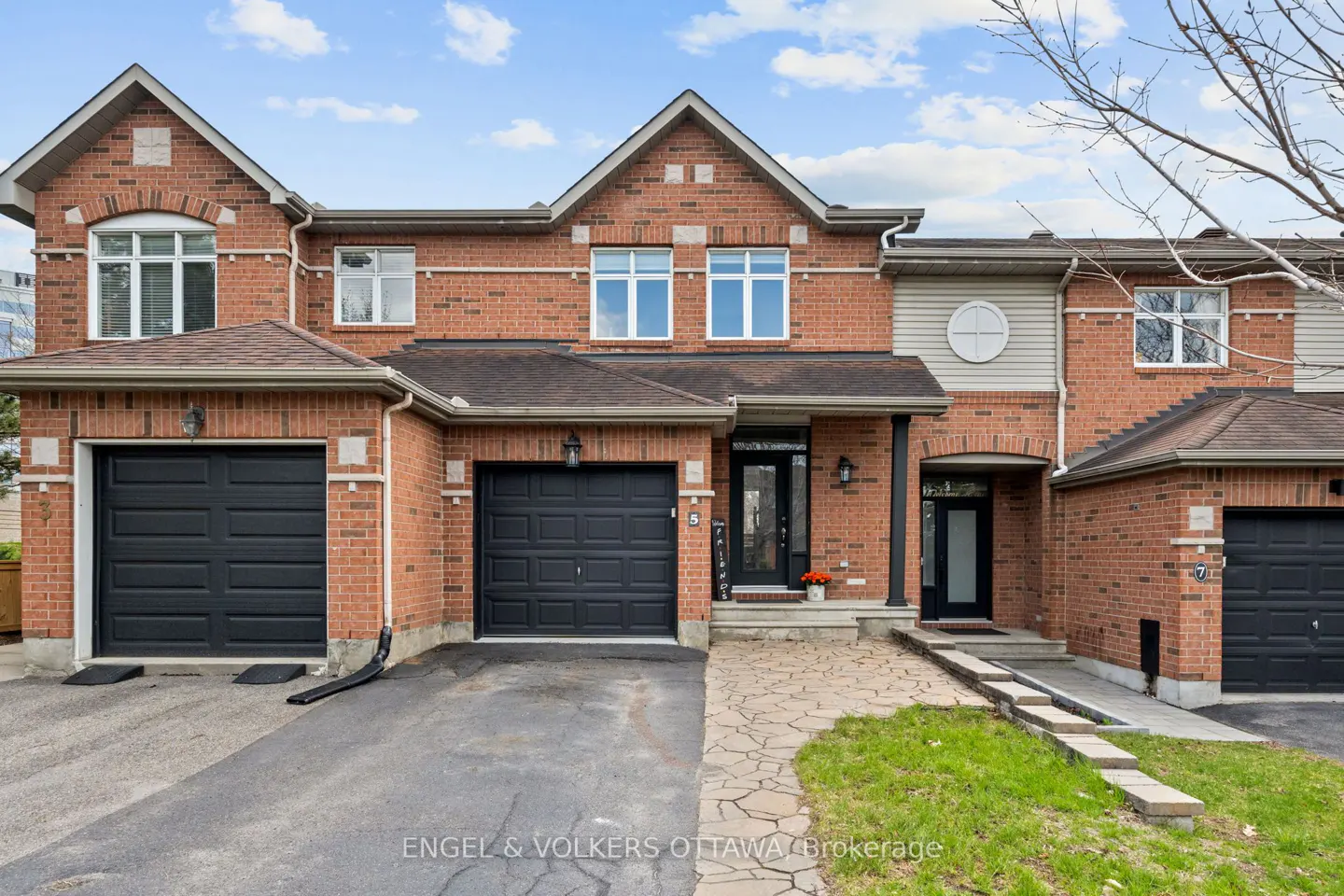 Exterior view of three attached brick townhouses with black garage doors and stone walkways.