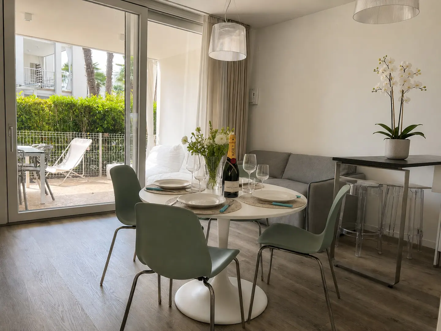 Interior view of a dining area with a round table set for four, a bottle of champagne, and a view to an outdoor patio.