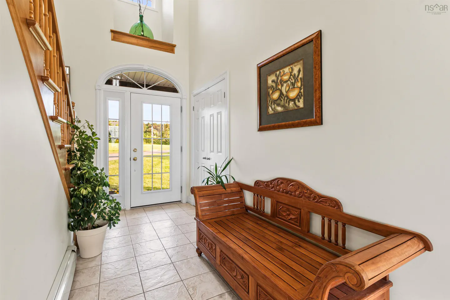 Foyer with white walls, tiled floor, wooden bench, and white double doors leading outside. A staircase is on the left.