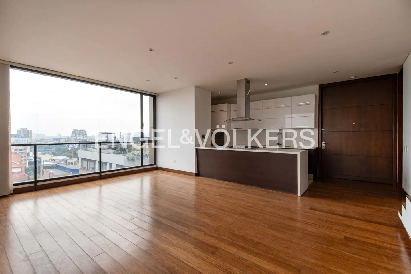 Bright, modern apartment with hardwood floors, a kitchen island, and a large window overlooking a city skyline.