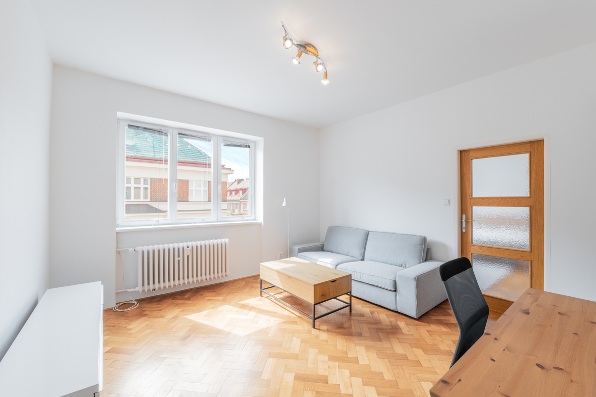 Bright room with herringbone wood floors, a light gray sofa, wooden coffee table, desk, and a window with city views.