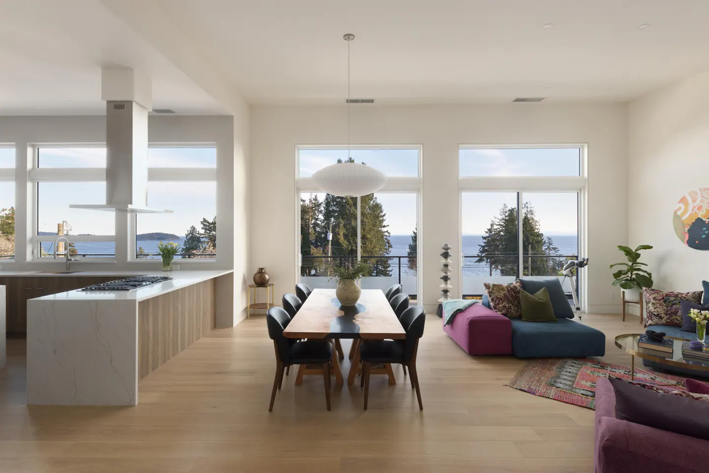 Bright, open-concept living space with a kitchen island, dining table, and colorful lounge area, all with a scenic ocean view.