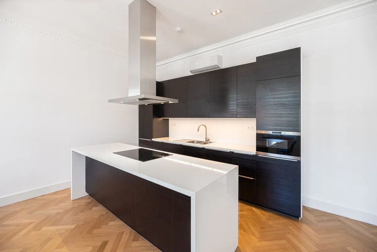 Modern kitchen with dark wood cabinets, white countertops, and stainless steel appliances. A kitchen island has a cooktop. Hardwood floors.