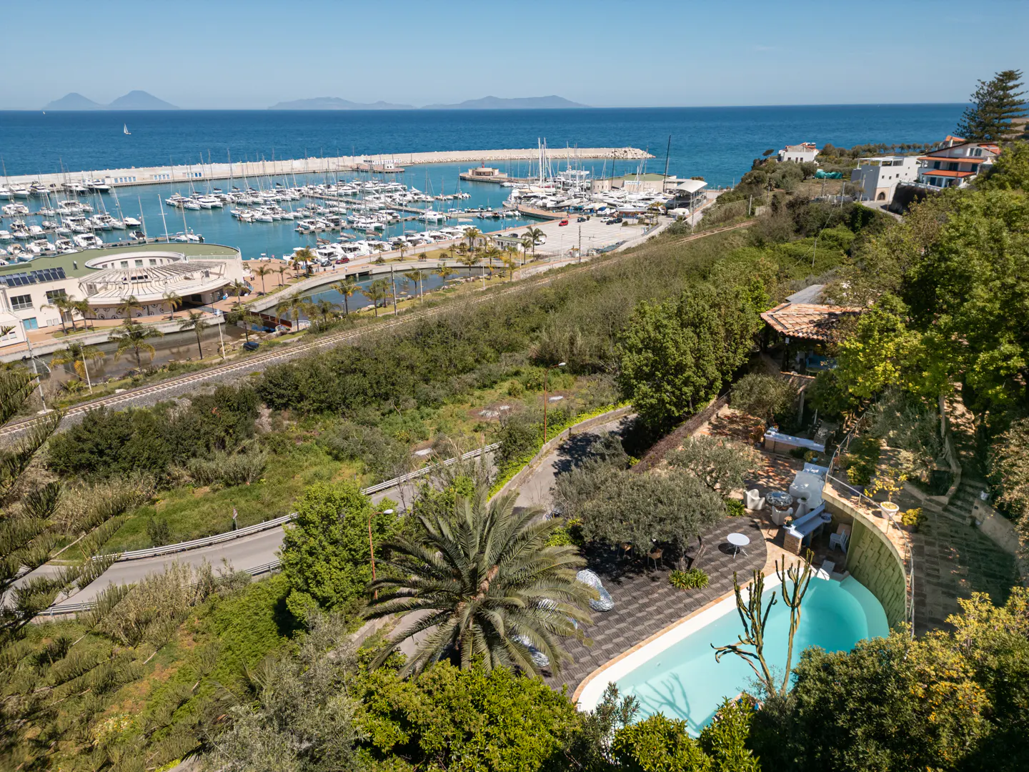 Scenic view of a marina filled with boats, a blue pool, and lush green trees on a sunny day.