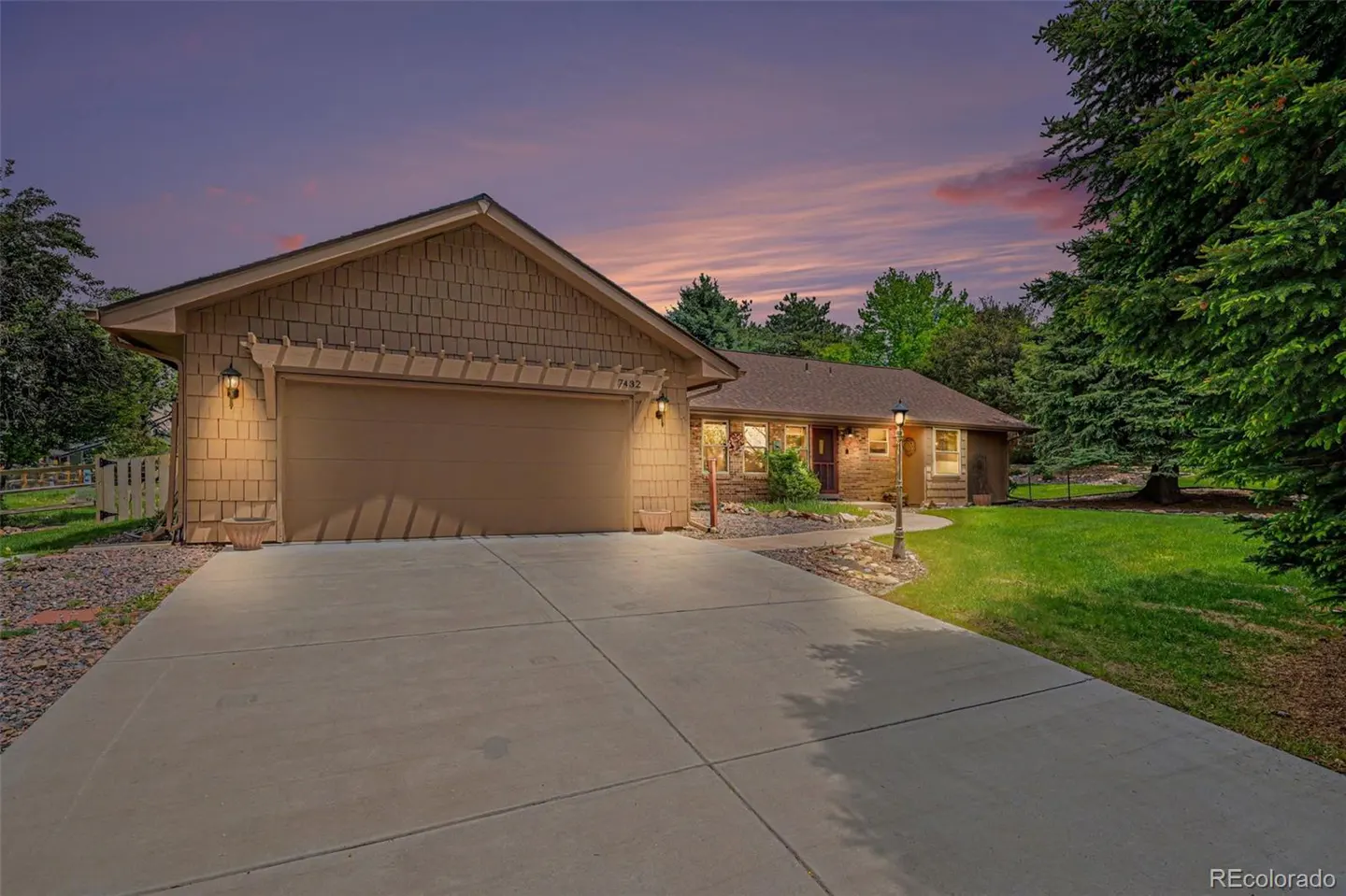 Exterior shot of a tan house with a large driveway, garage, and green lawn at dusk.