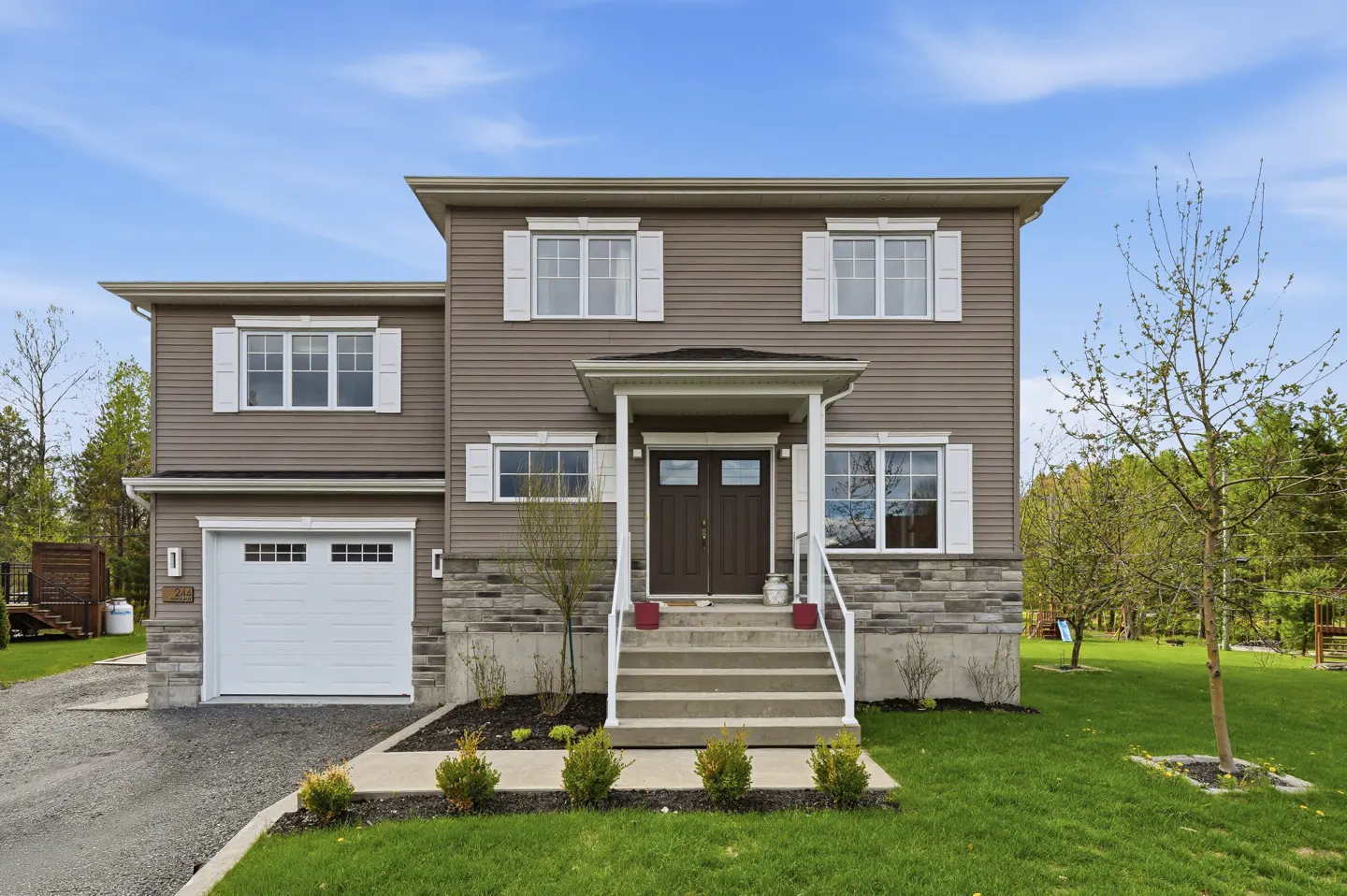 Two-story house with brown siding, white trim, and a white garage door. A stone foundation and green lawn add to the curb appeal.