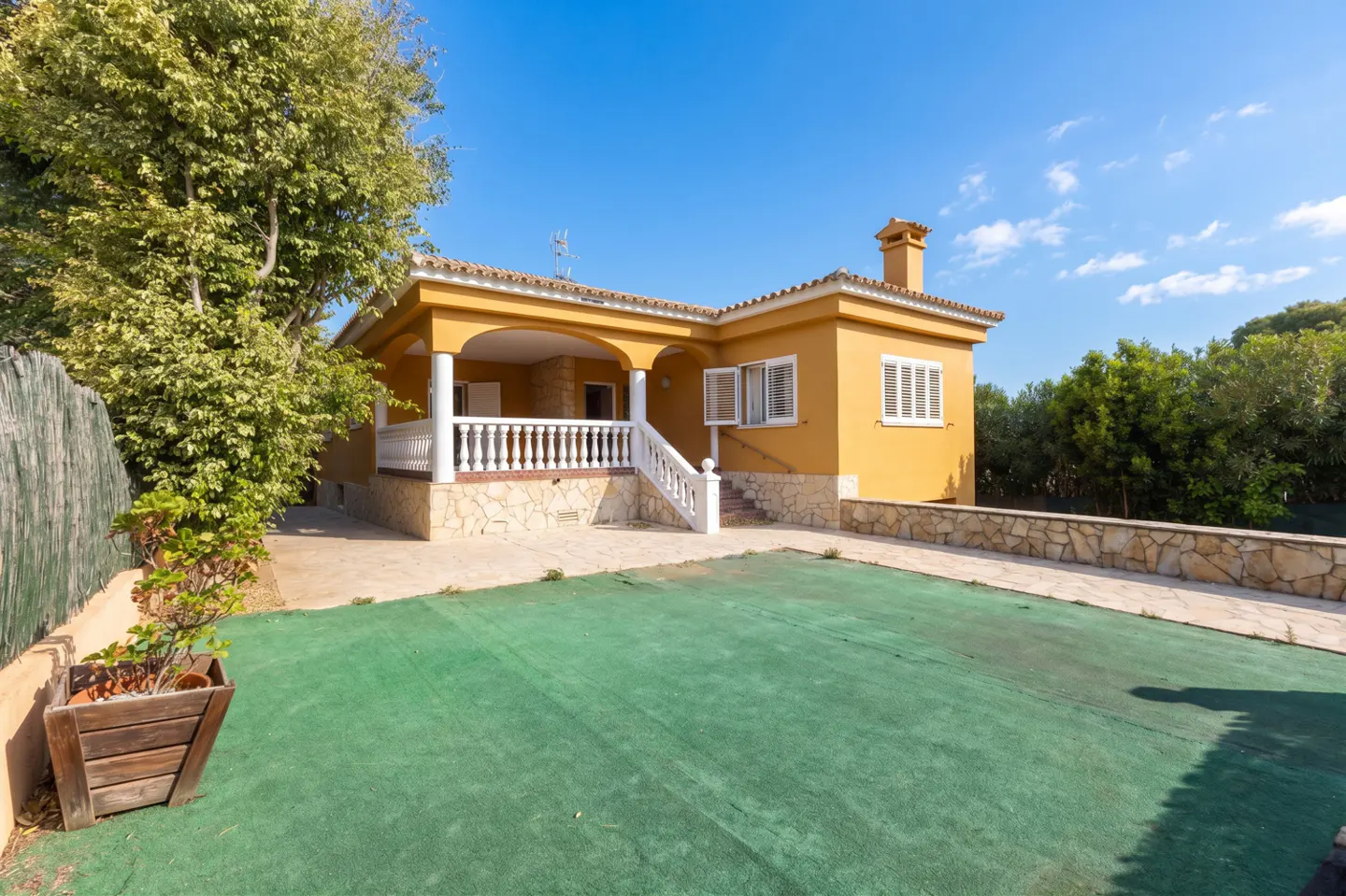 A yellow house with a white porch and green lawn under a blue sky.
