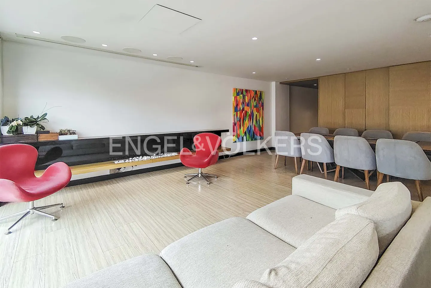 A modern living room with a white sofa, red chairs, a black fireplace, and a dining table with gray chairs.