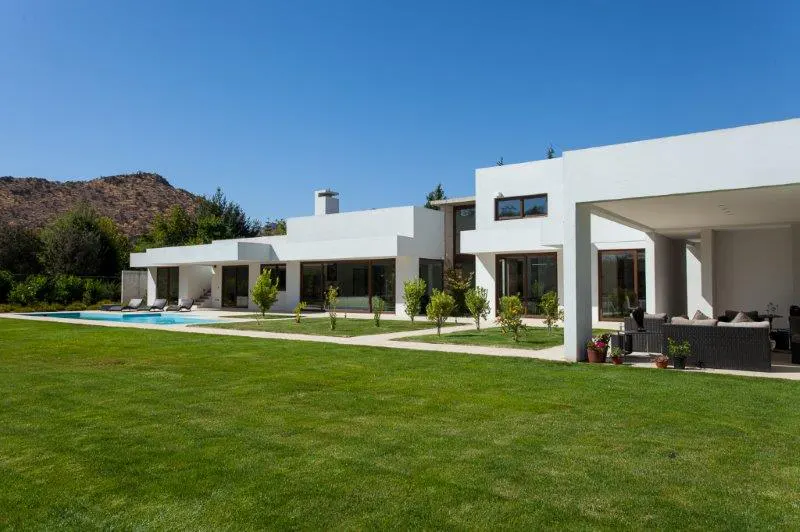 Modern white house with a pool and green lawn under a clear blue sky. A mountain is visible in the background.