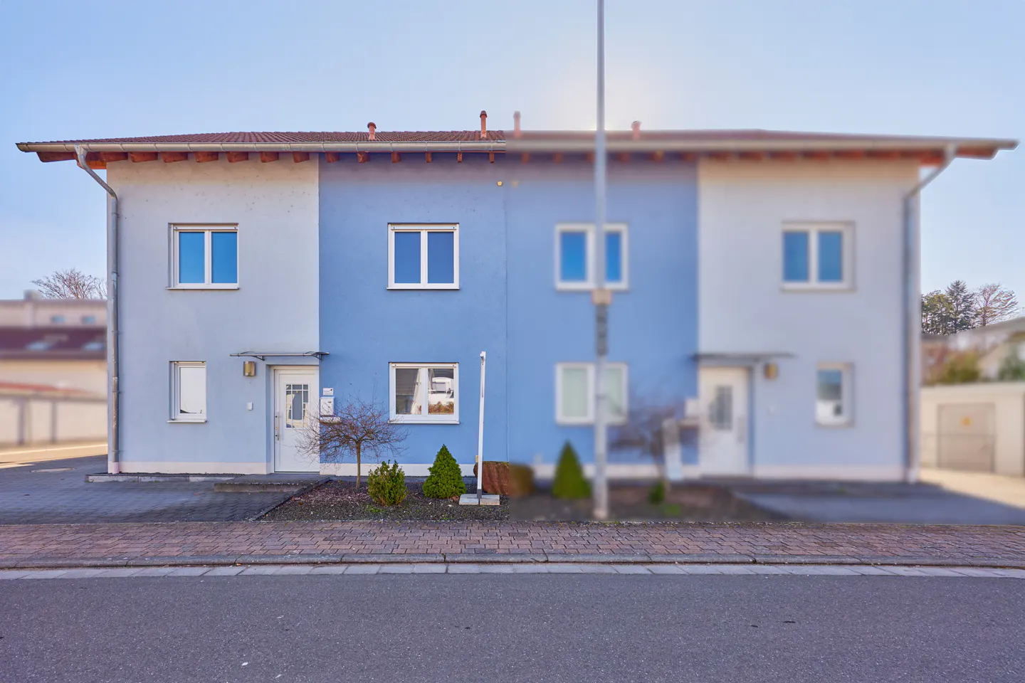 Two-story duplex with light blue and blue facades, white doors, and a red-tiled roof.