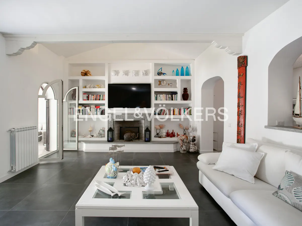 Bright living room with white sofa, coffee table, and built-in shelves featuring a TV and fireplace on dark tile floors.