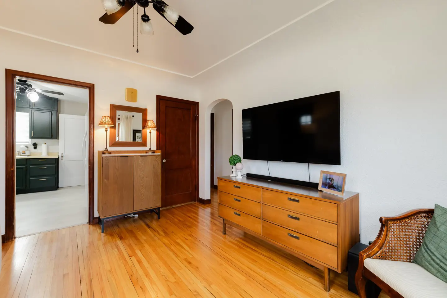 Living room with wood floors, a TV on a dresser, and a view into a kitchen.