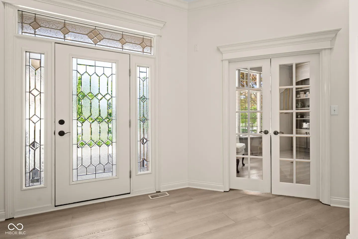 Bright foyer with white walls, light wood floors, and two white doors with glass panels.