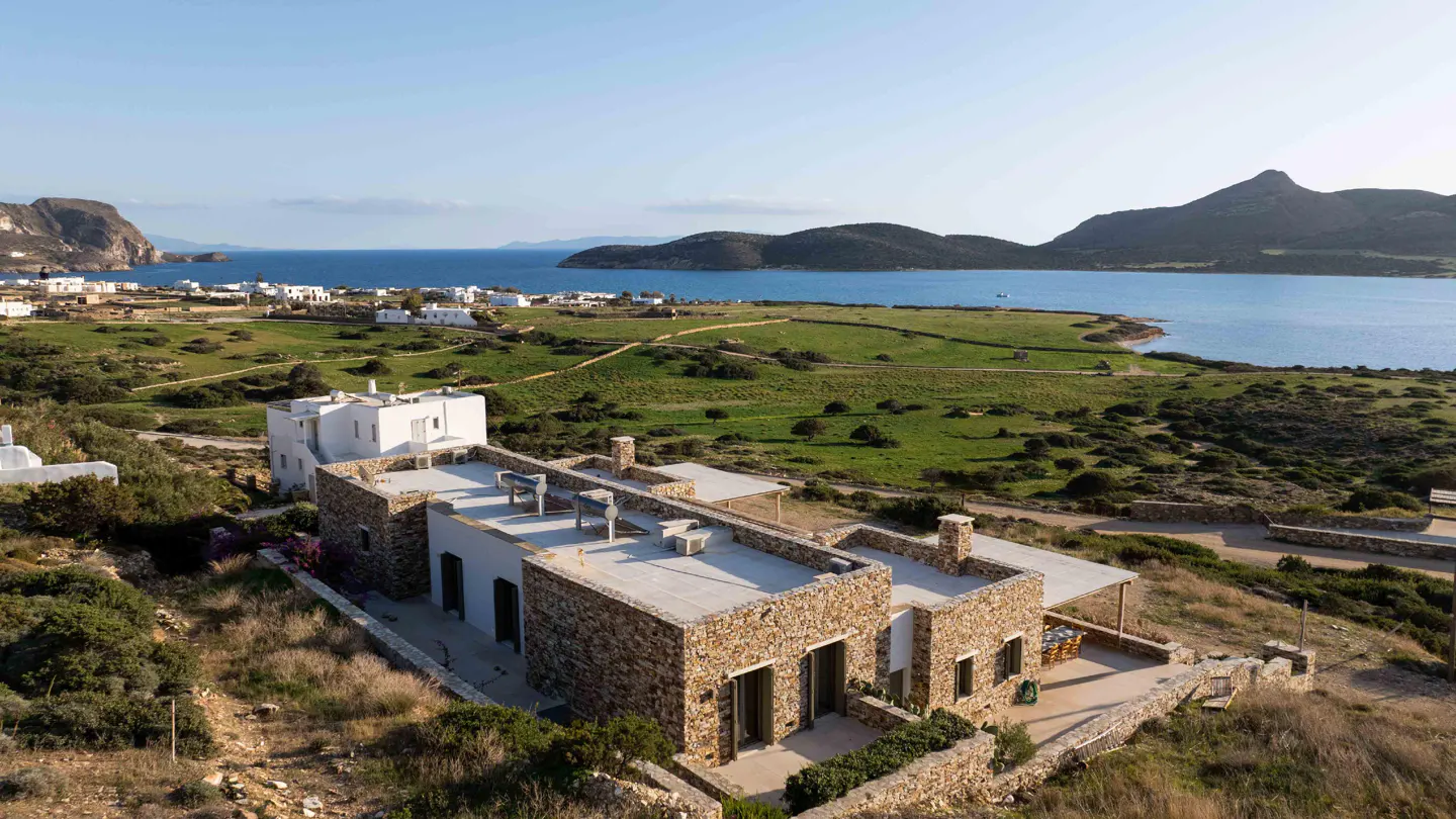 Stone house with a flat roof overlooking the ocean and a town in the distance.