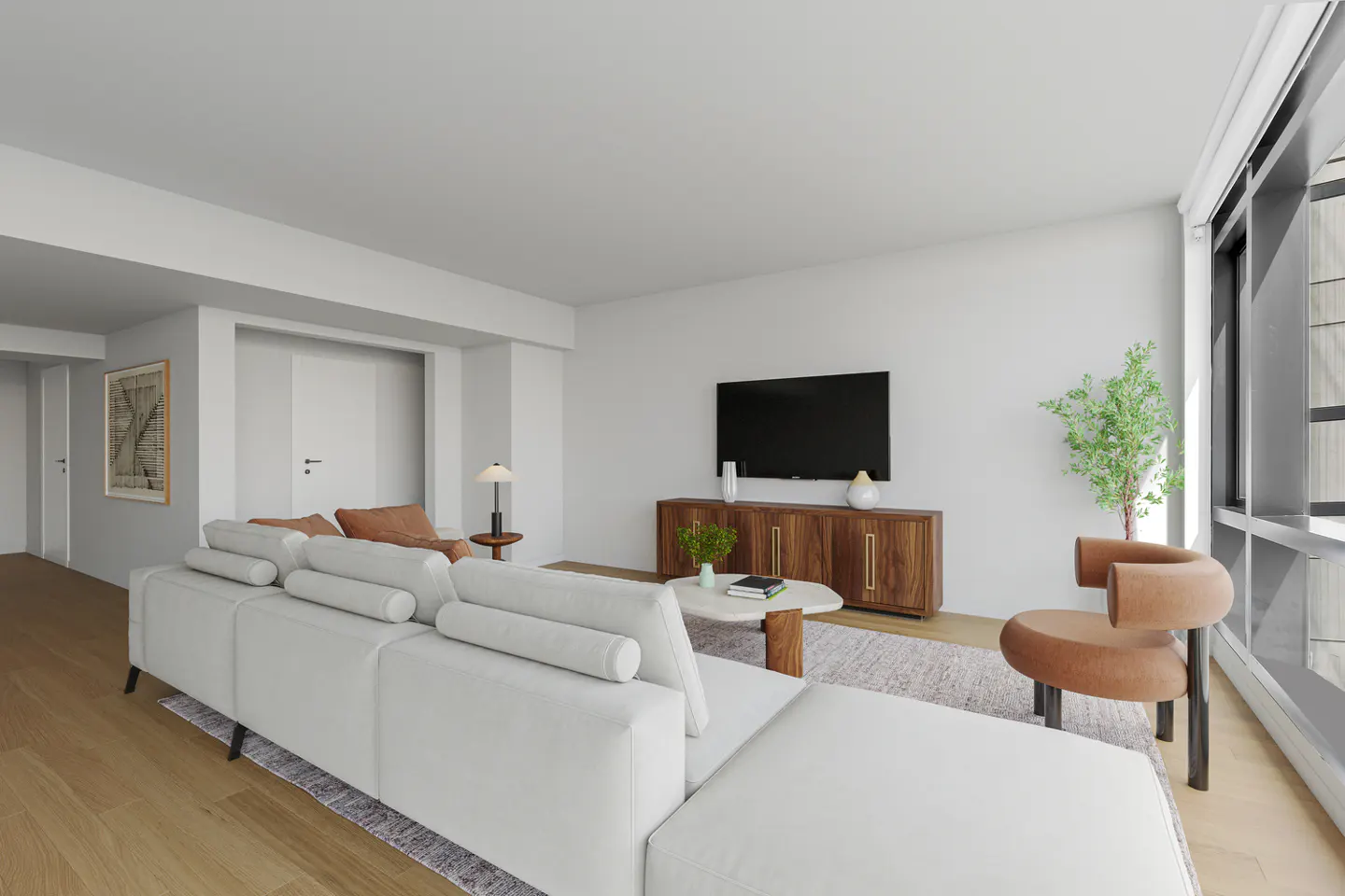Bright living room with a white sectional sofa, wood floors, and a large window. A brown chair sits near a potted plant. A TV is mounted above a wooden cabinet.