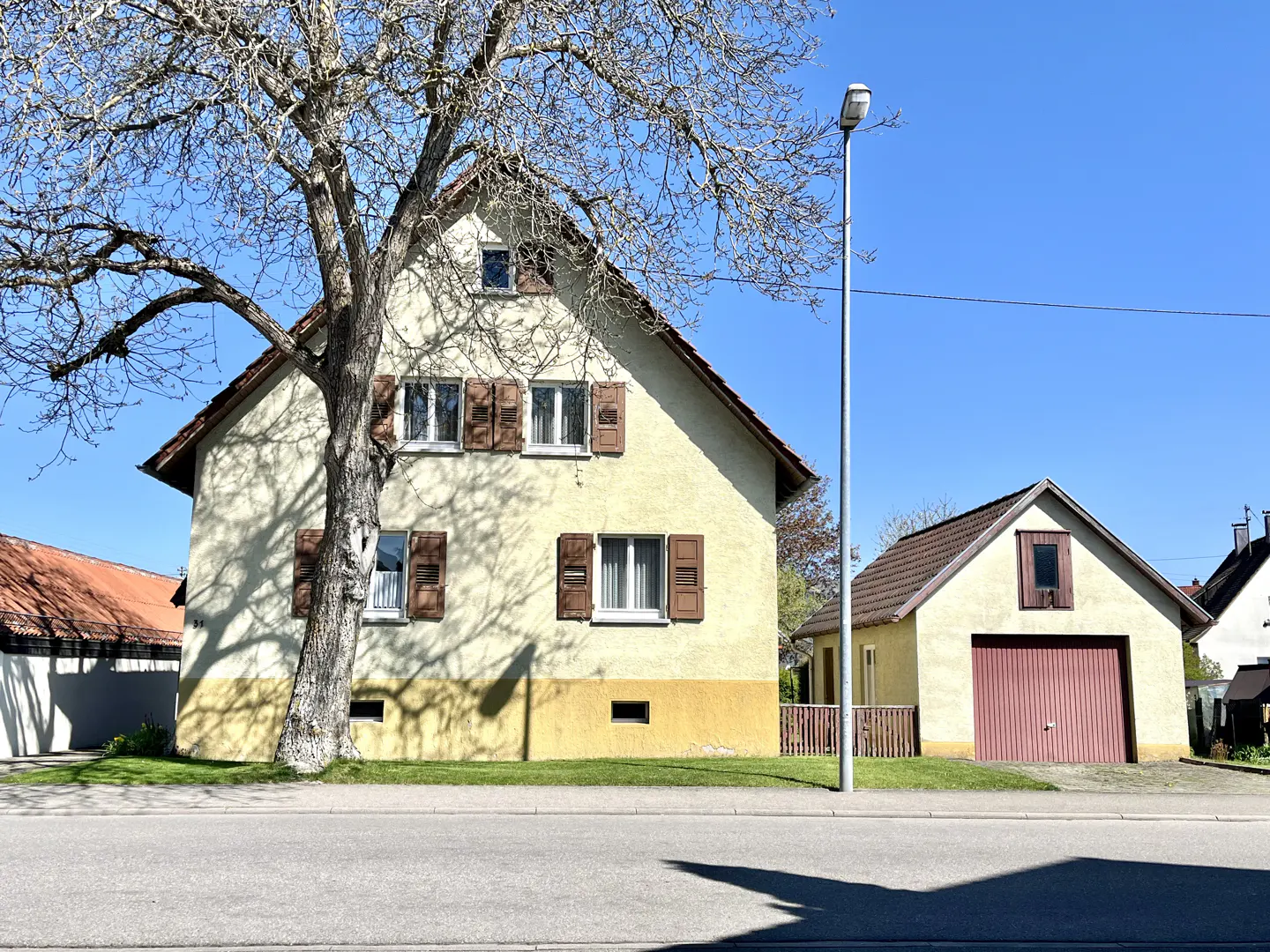 Two-story yellow house with brown shutters, next to a garage with a red door, under a blue sky.