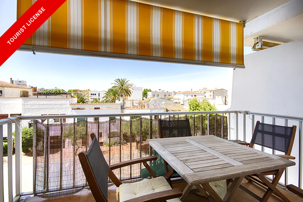 Balcony view with a wooden table, chairs, and a yellow striped awning. Cityscape with palm trees in the background.