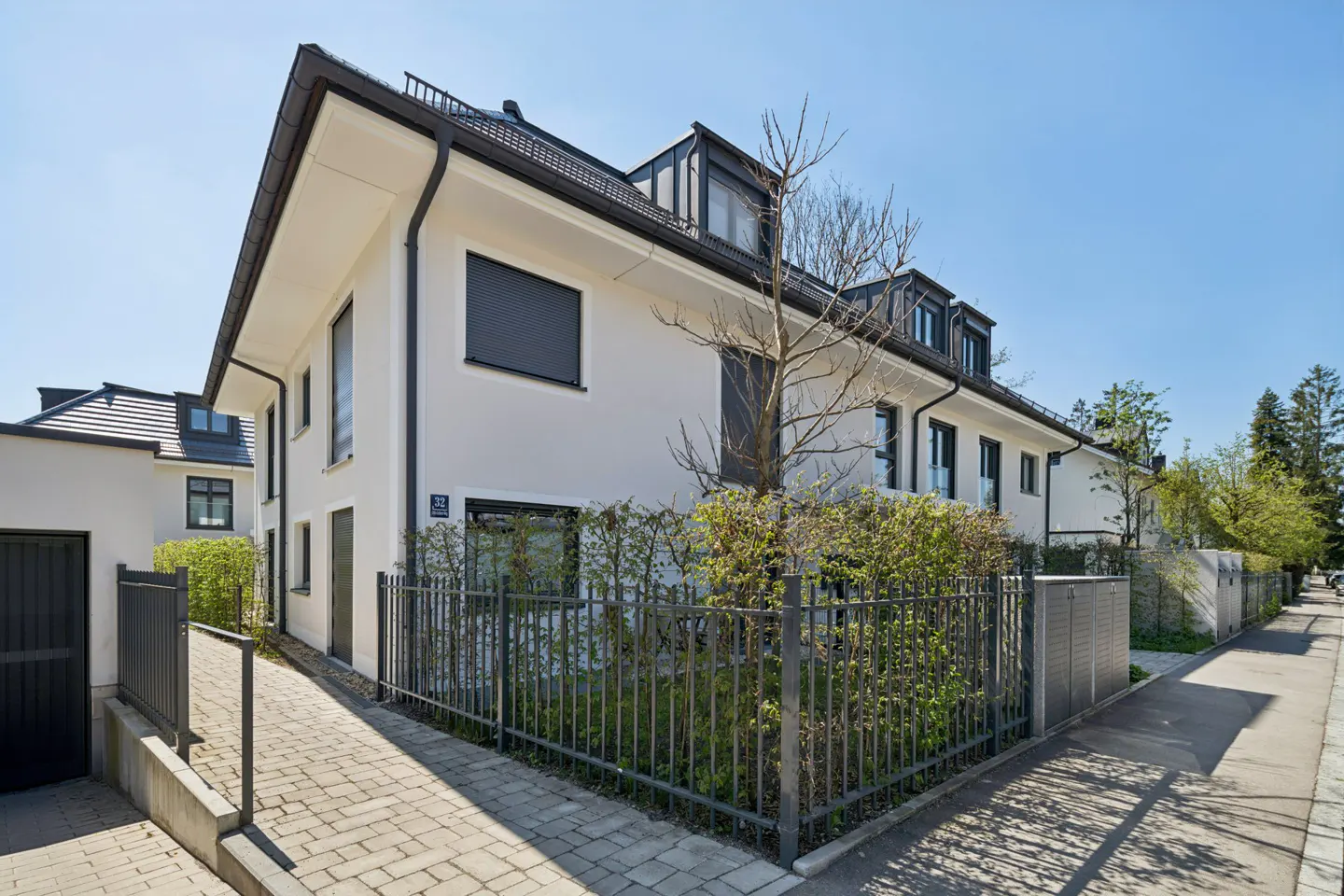 Exterior of a modern, two-story white house with black trim and a metal fence. A brick walkway leads to the entrance.