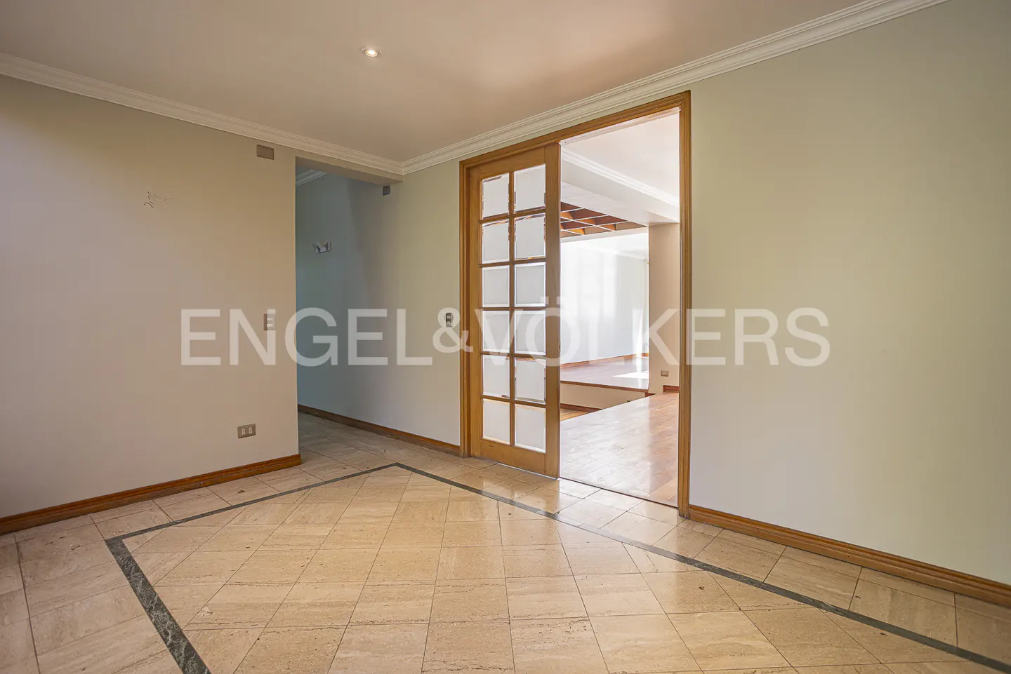 Empty room with light-colored walls, beige tiled floors with dark borders, and a wooden sliding door leading to a hallway.