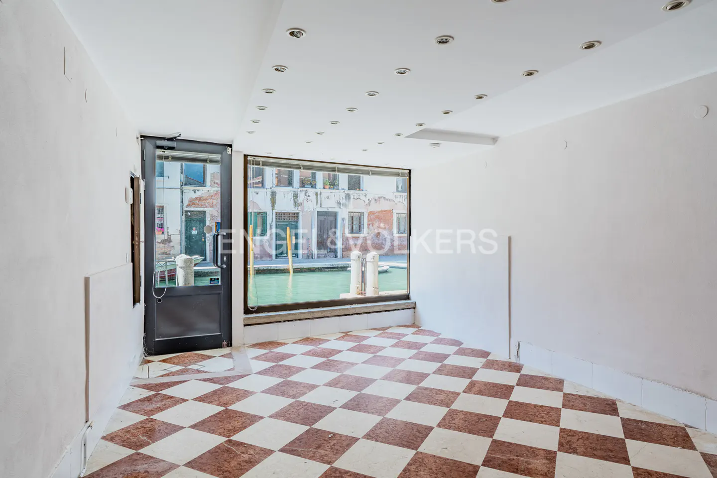 Empty room with red and white checkered floor, white walls, and a window overlooking a canal in Venice.