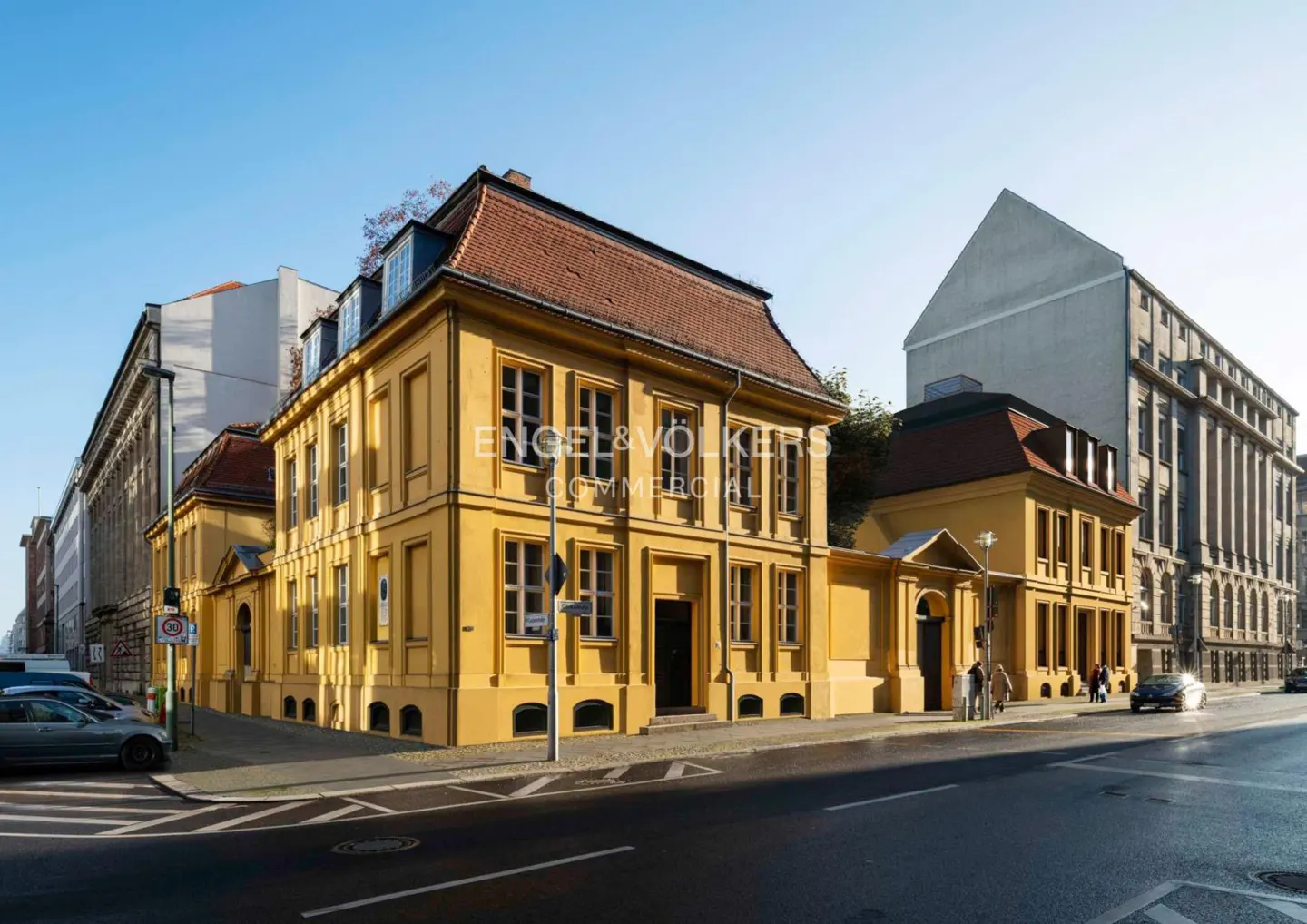 Exterior view of a yellow, two-story commercial building with a red tile roof on a city street.