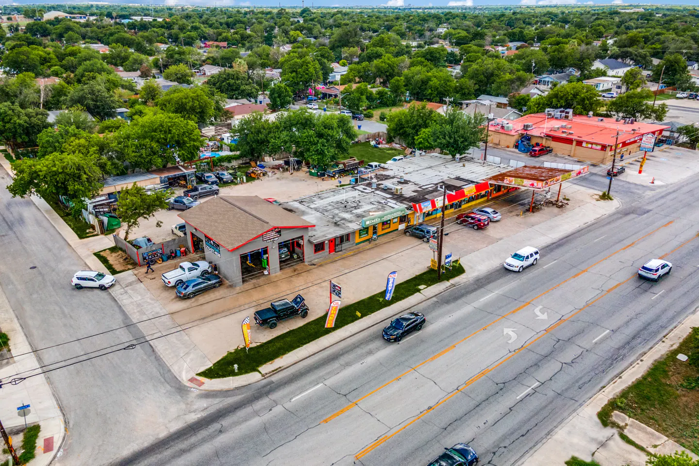 Aerial view of a commercial property with a gray auto shop, a red-roofed building, and a gas station on a busy street.