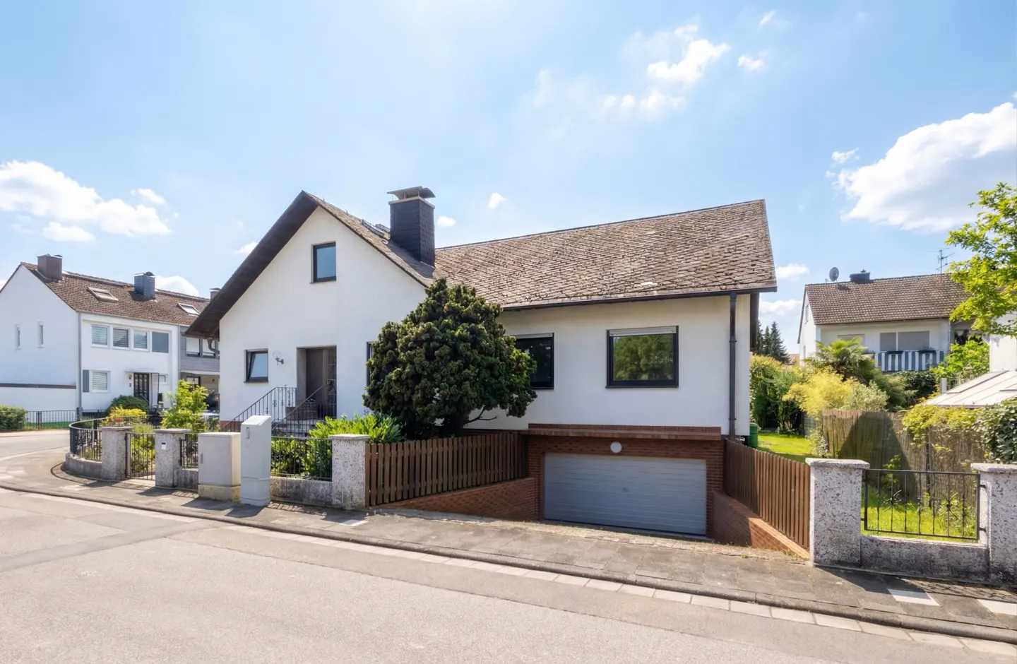Exterior view of a two-story white house with a gray garage door and a brown roof on a sunny day.