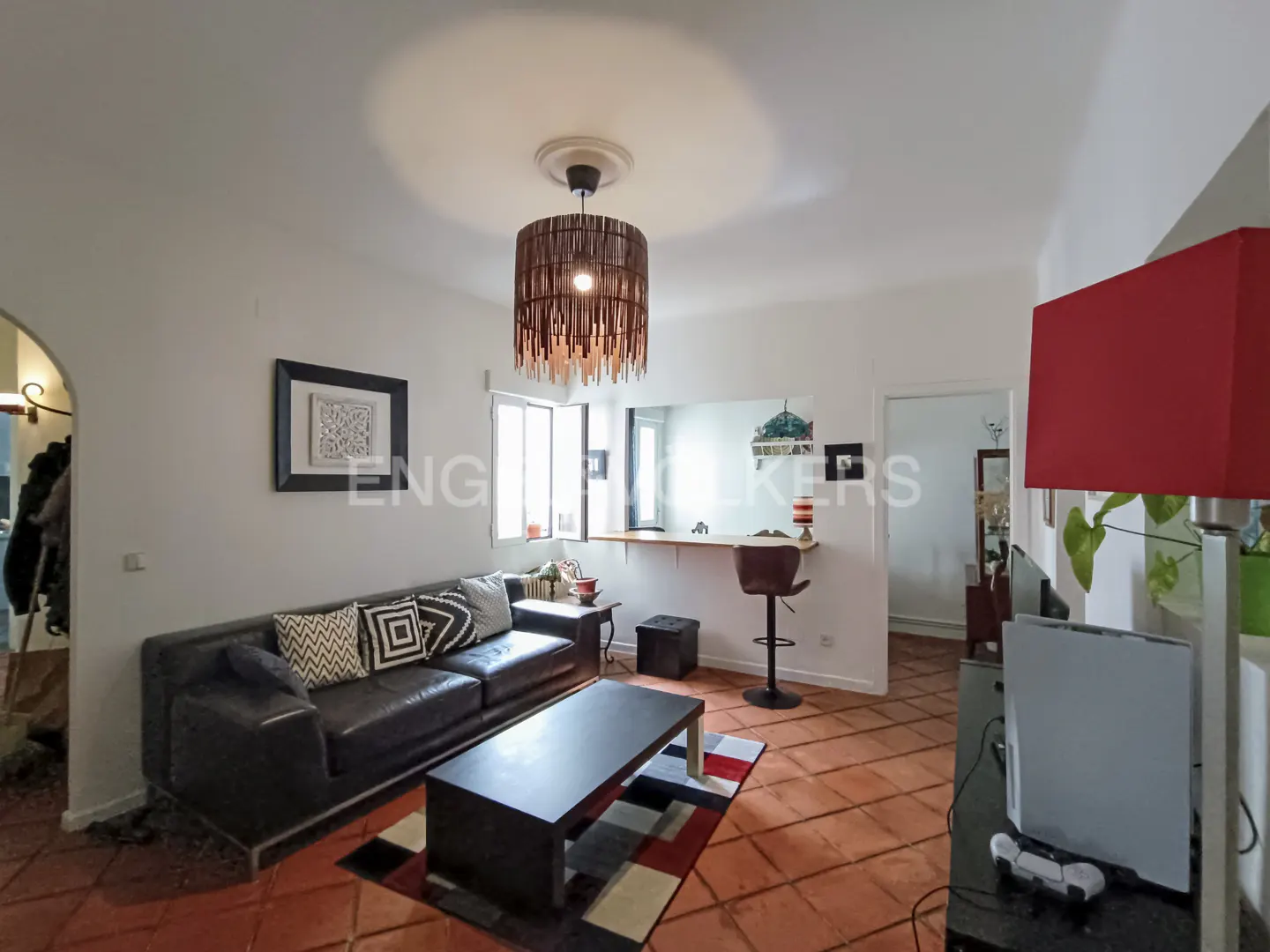 Living room with dark leather sofa, coffee table on a patterned rug, breakfast bar, and a unique fringed pendant light.