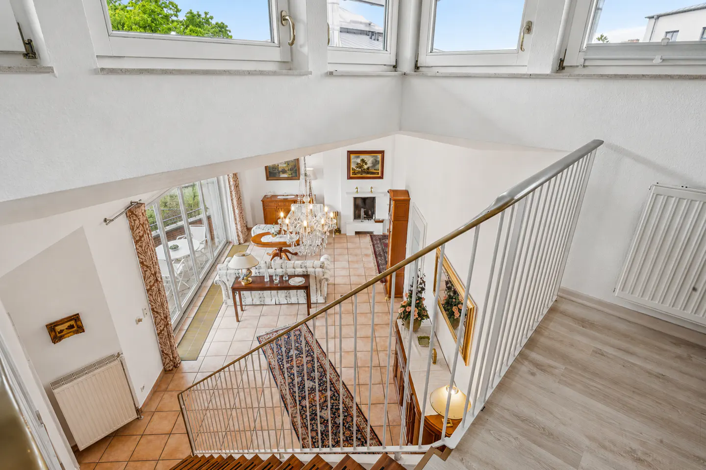 High-angle view of a bright living room with tile floors, a crystal chandelier, fireplace, and a white metal staircase.