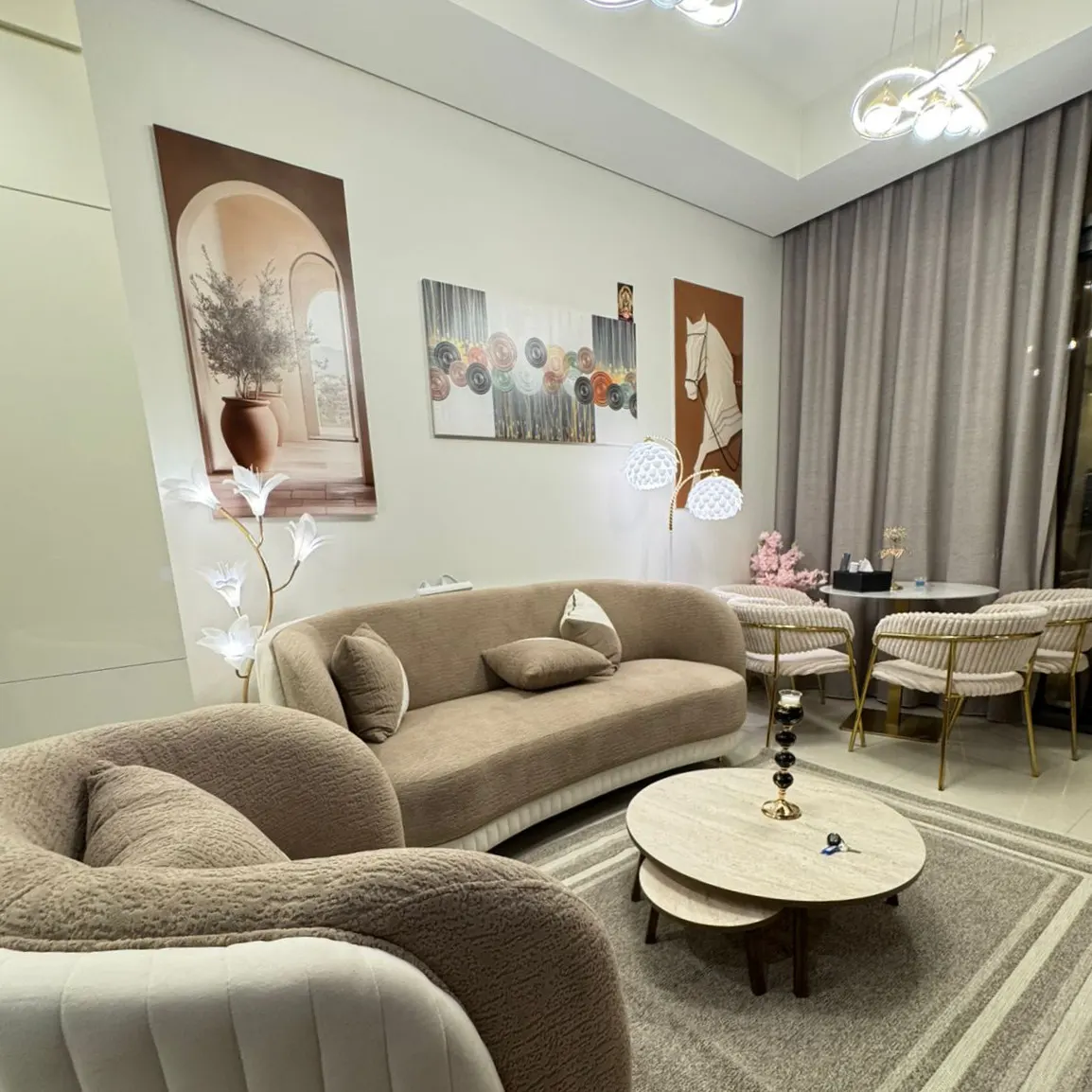 Living room with beige sofas, round tables, and art. Neutral color palette, modern lighting, and a gray rug create a cozy atmosphere.