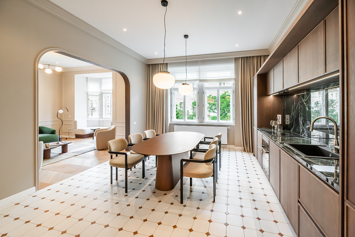 Modern kitchen and dining area with a wooden table, beige chairs, marble backsplash, and an arched doorway to a living room.