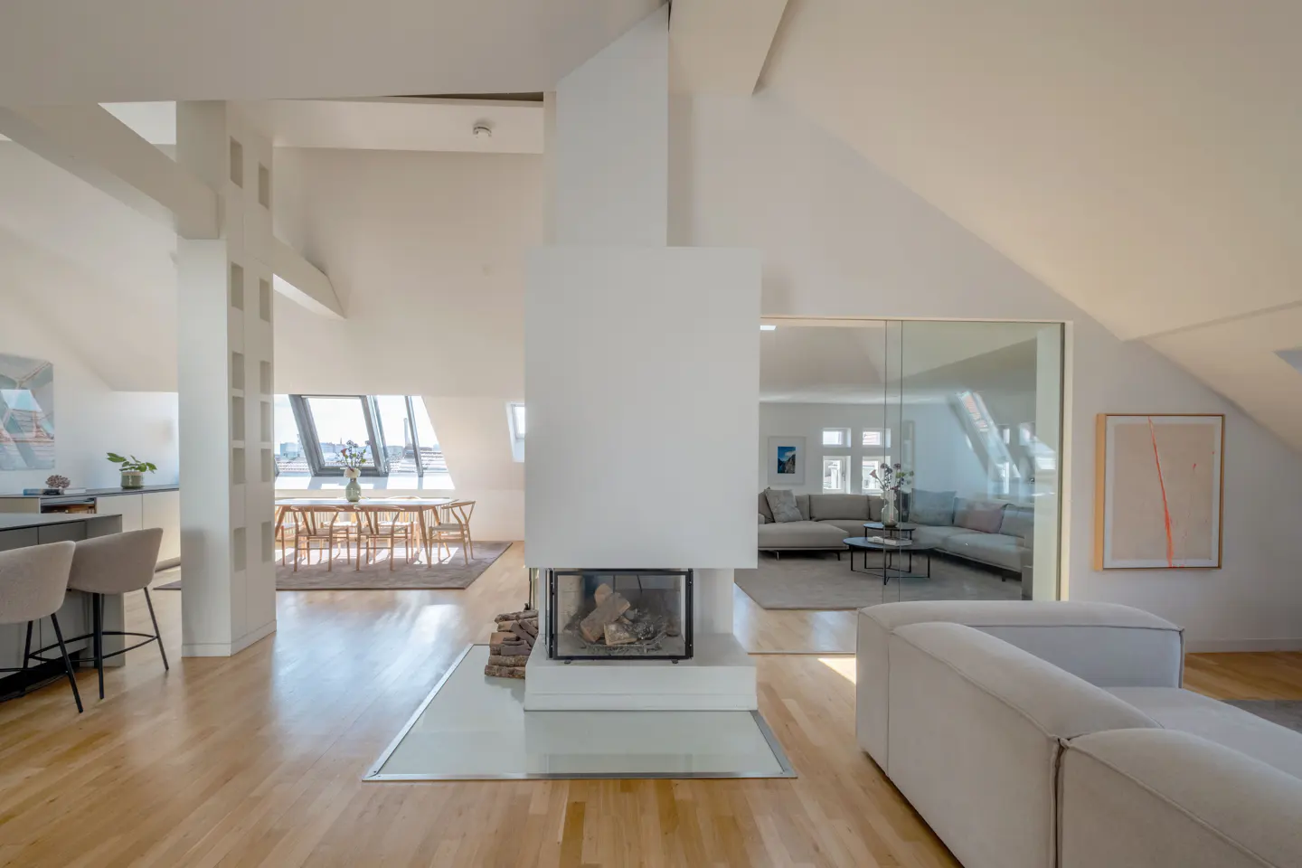 Bright, open-concept living space with hardwood floors, a white fireplace, and a dining area with a view. A glass wall separates the living room.