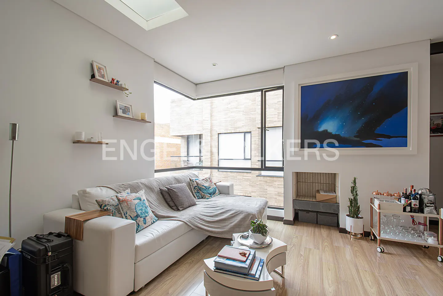 Bright living room with white sofa, throw pillows, and a blanket. Large windows, art, and a bar cart add to the modern decor.