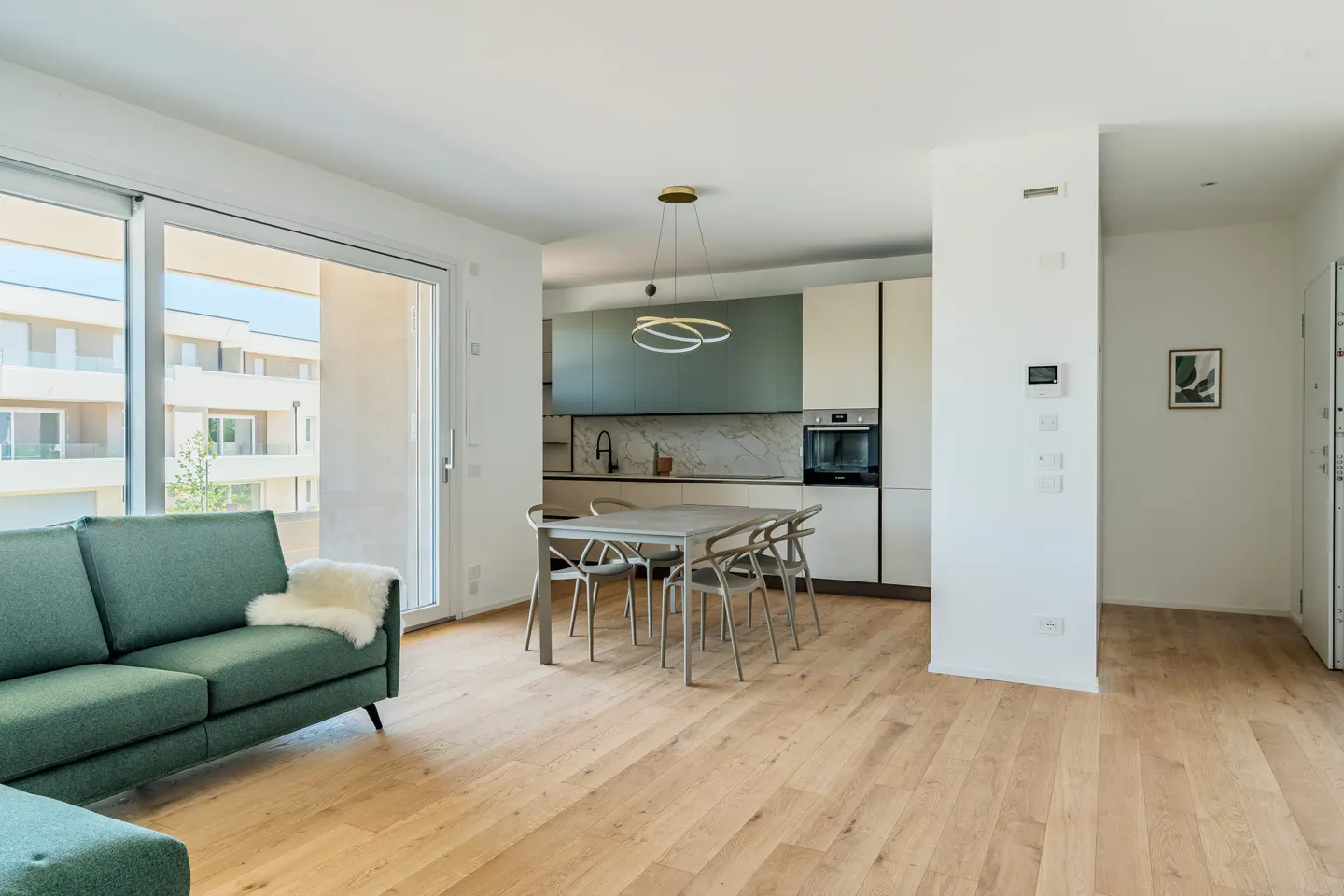Bright, modern apartment interior with a green sofa, dining table, and kitchen with white and green cabinets. Hardwood floors add warmth.
