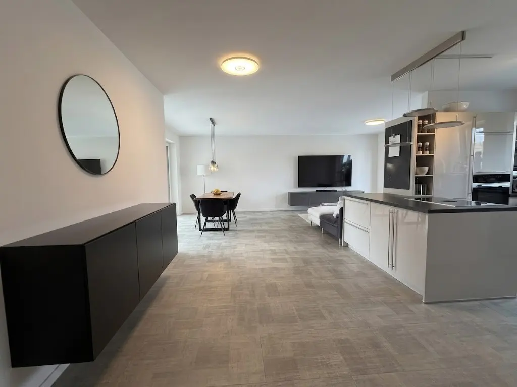 Open-concept living space with a black console, round mirror, dining table, TV, and a white kitchen island.