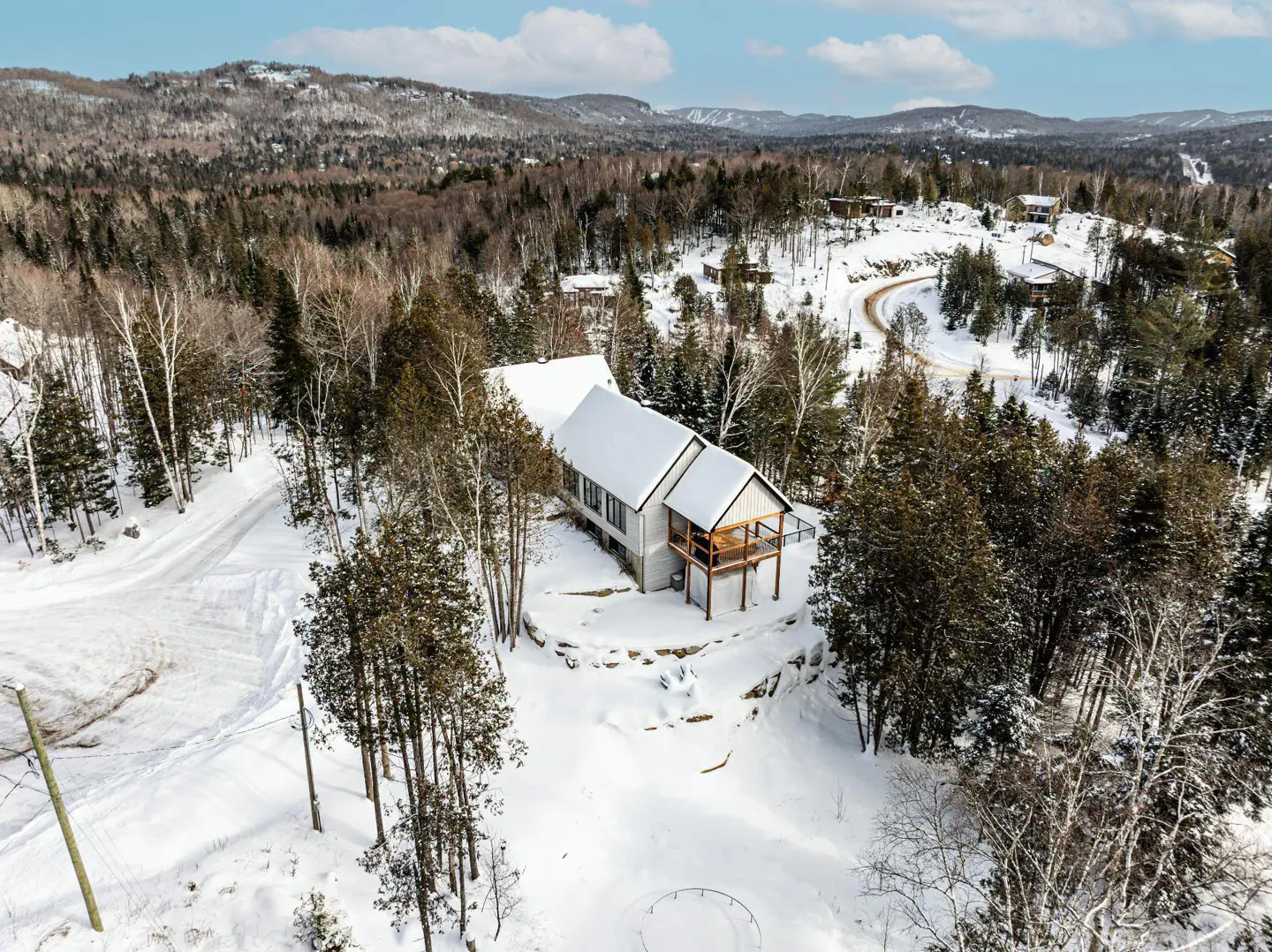 Aerial view of a snow-covered house with a balcony, surrounded by trees and a snowy landscape.