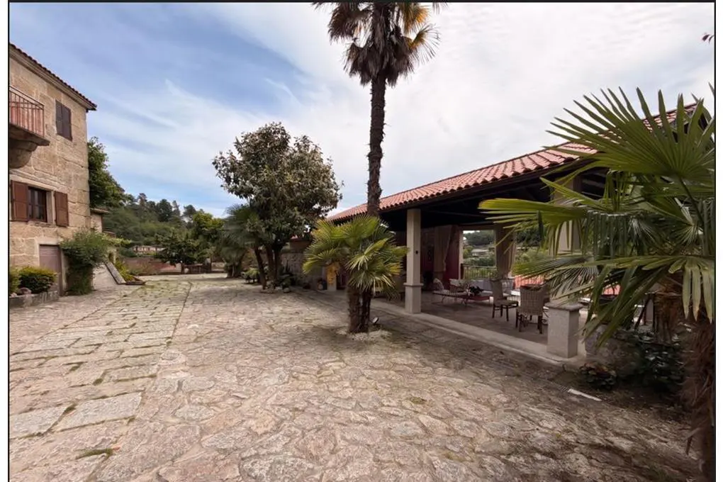 Stone courtyard with palm trees leads to a covered patio with seating. A stone building is on the left.