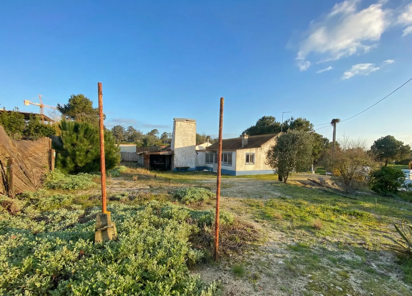 Exterior view of a one-story house with a tall chimney, surrounded by green vegetation under a blue sky.