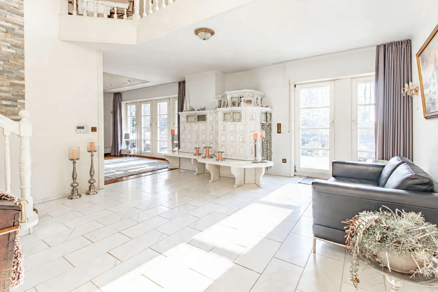Bright, airy foyer with white tile floors, a black leather sofa, and a white tiled fireplace. French doors lead to a sunlit room.